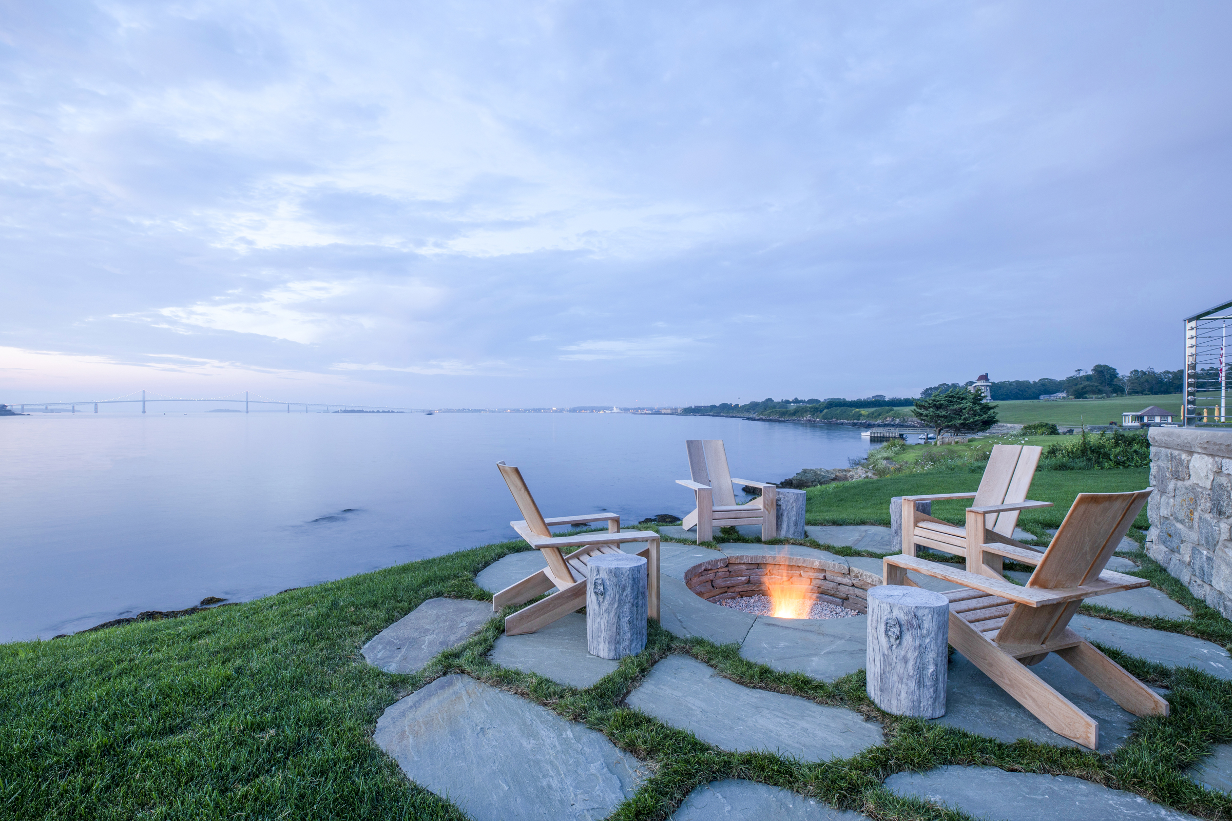 Adirondack chairs circle a fire pit at the edge of Narragansett Bay