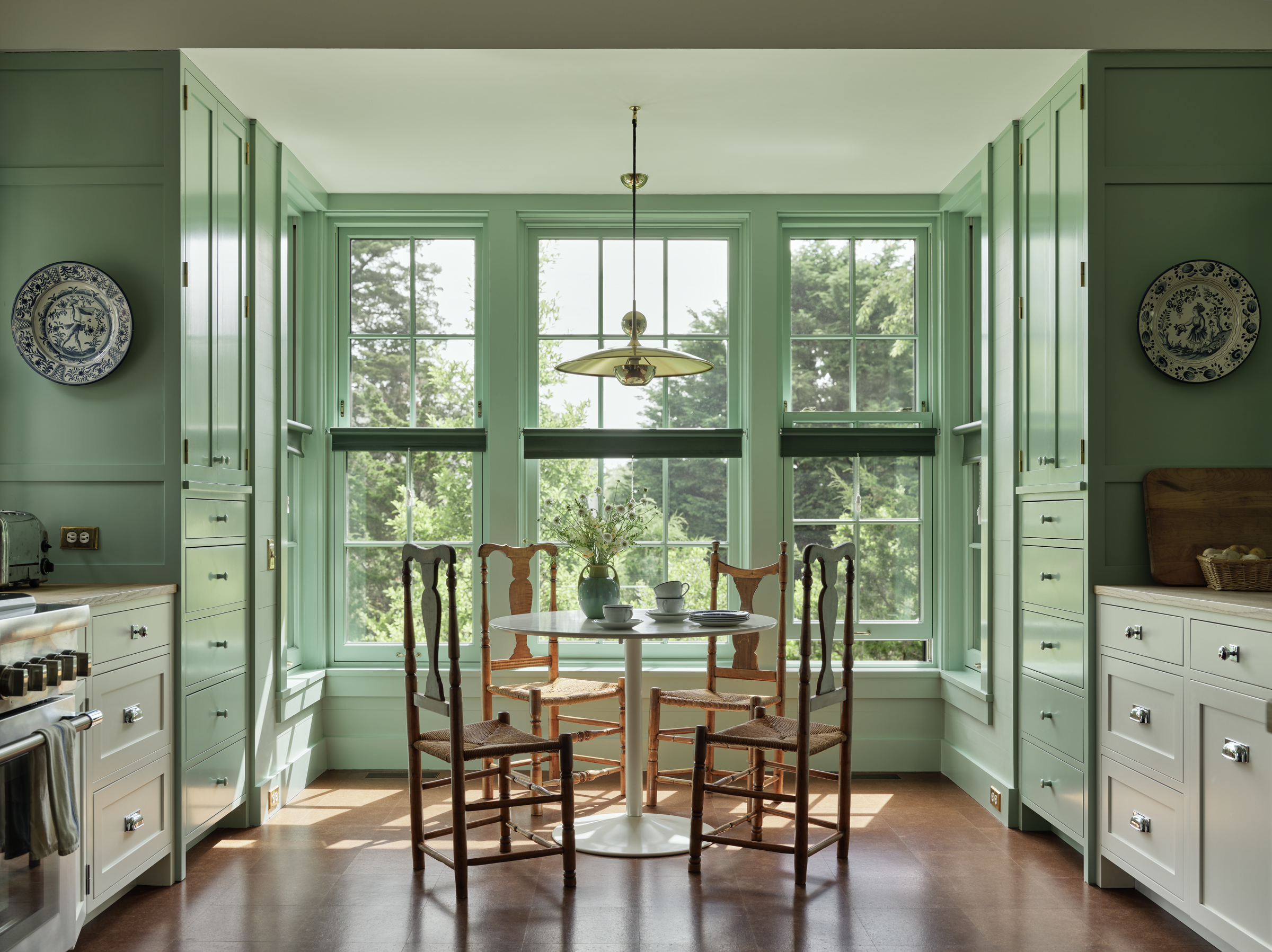 Green-painted kitchen casework surrounds a sunny bay with an antique breakfast table