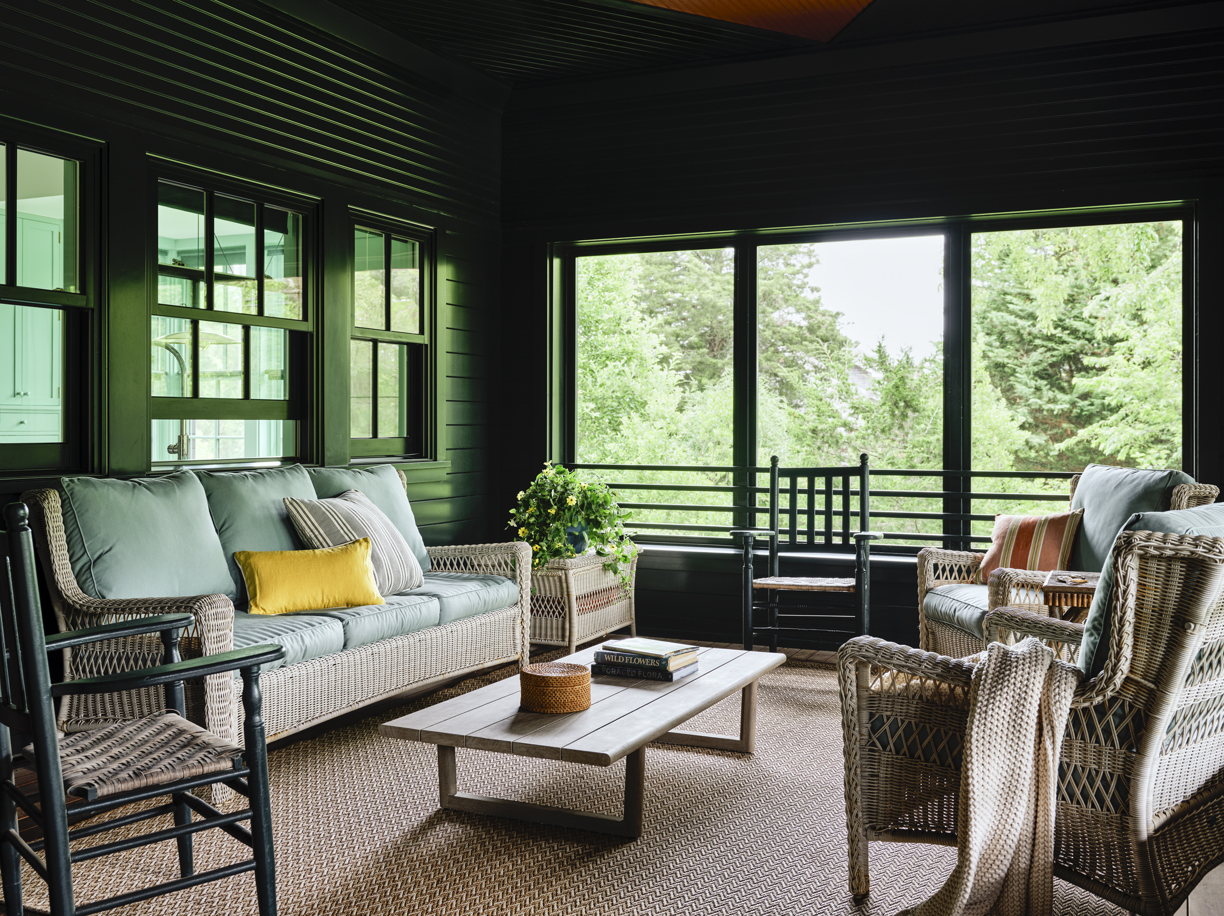 A dark green screened porch opens to the wooded landscape