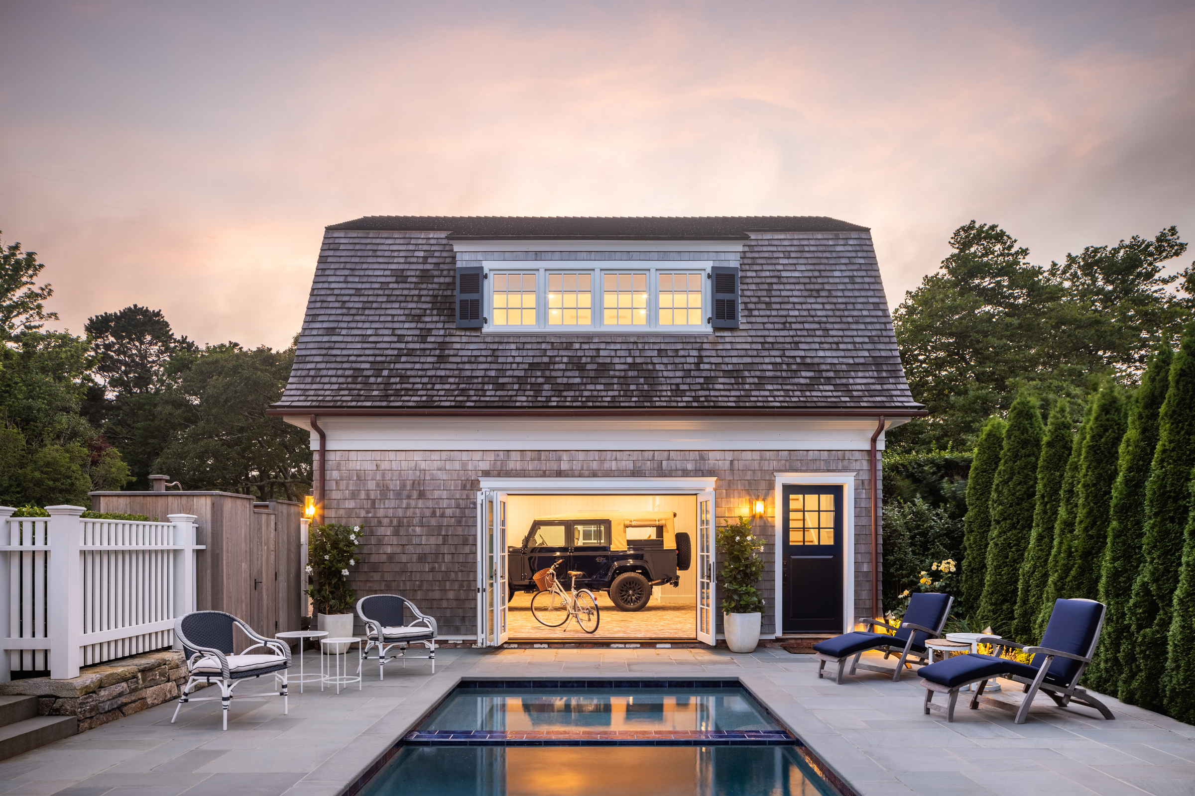 The carriage-house garage opens as a poolside cabana beside the bluestone terrace at dusk