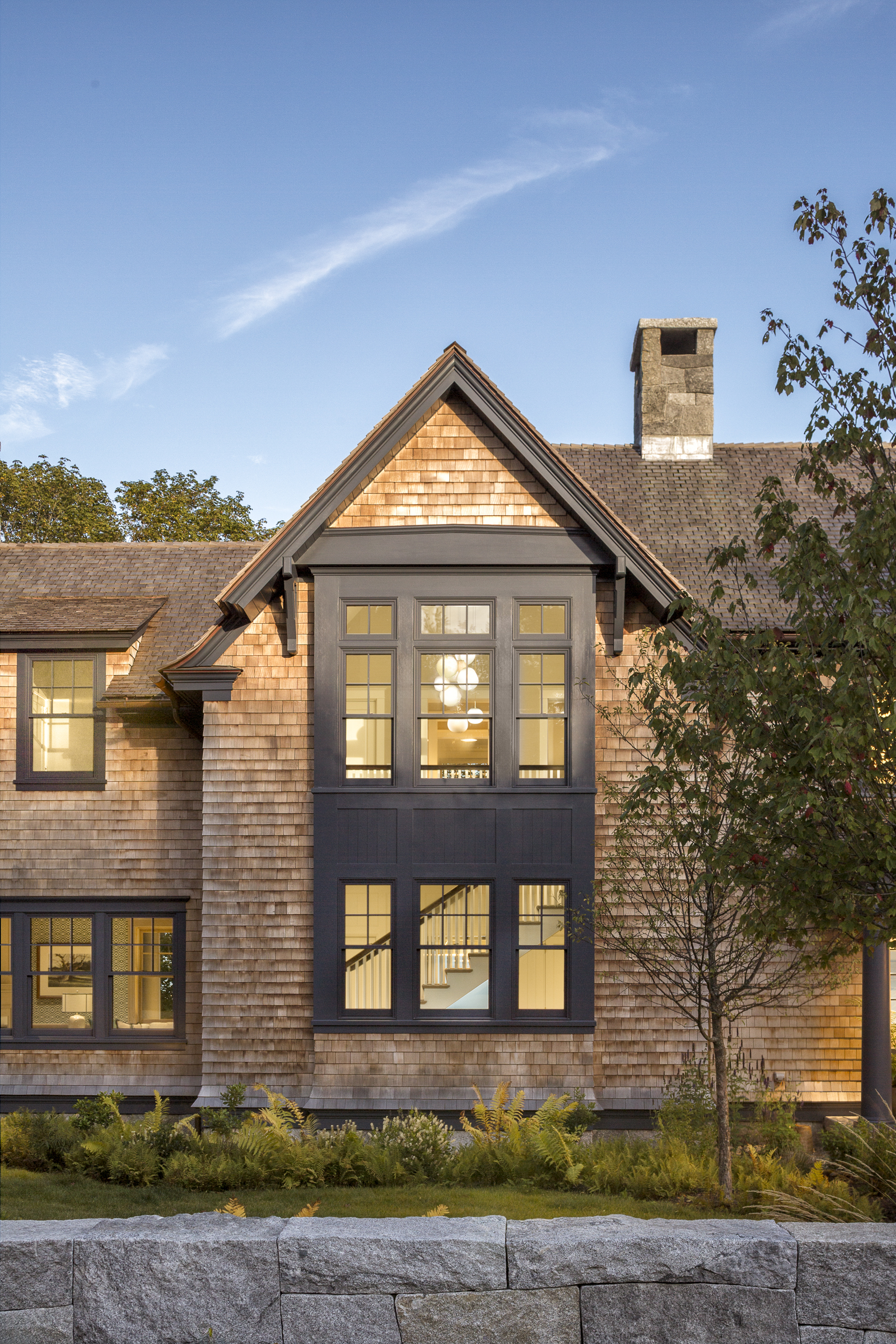 A projecting bay stacks windows across two floors of the cedar-shingled house
