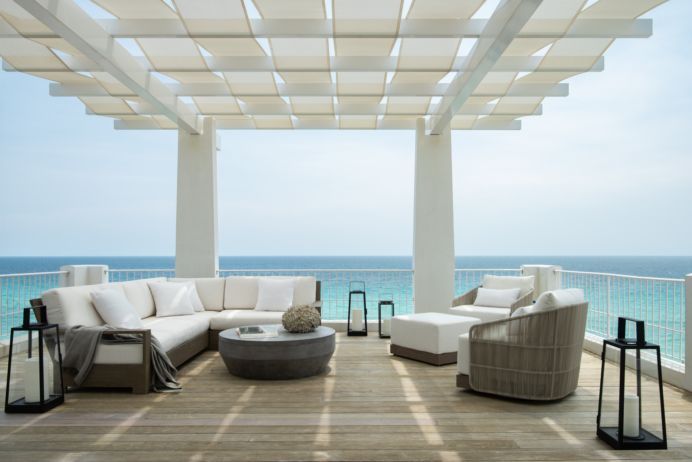 A white pergola filters sun over a grey-toned teak rooftop seating area