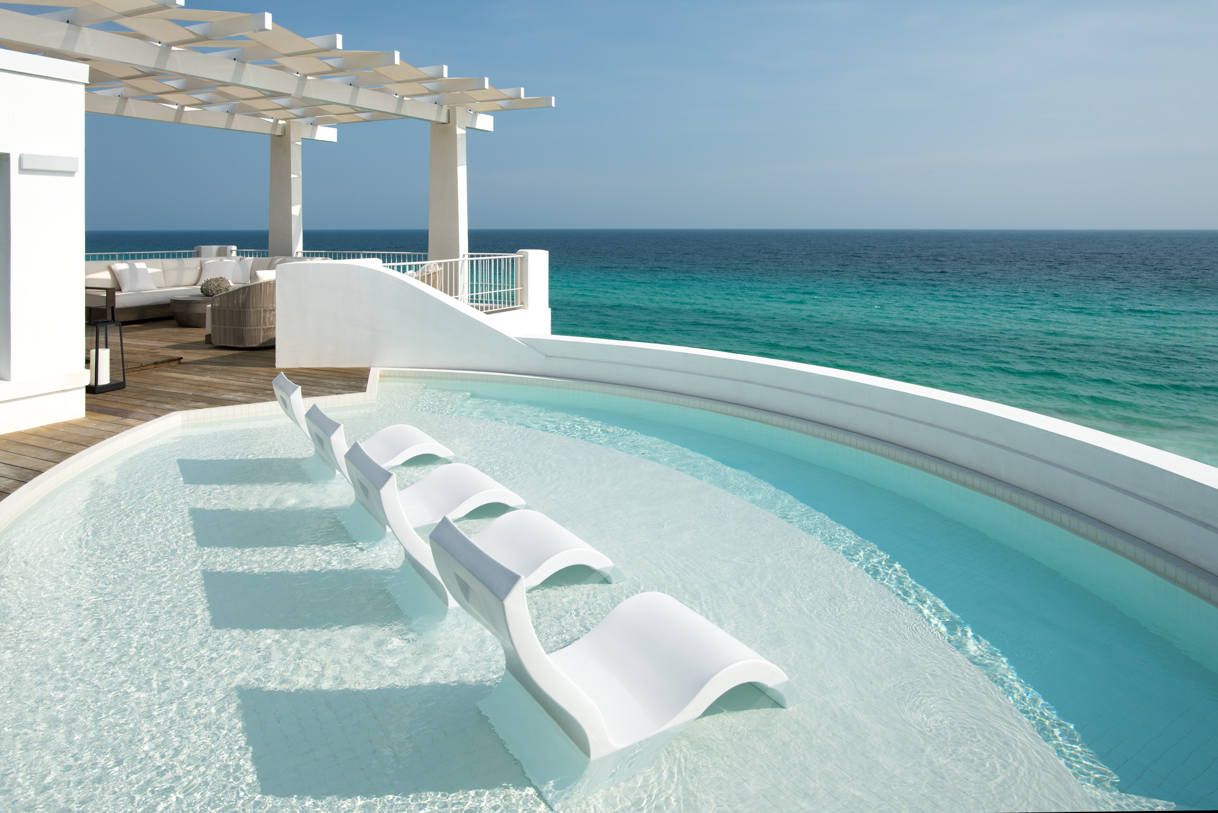 White in-water loungers face the Gulf from a shallow rooftop pool