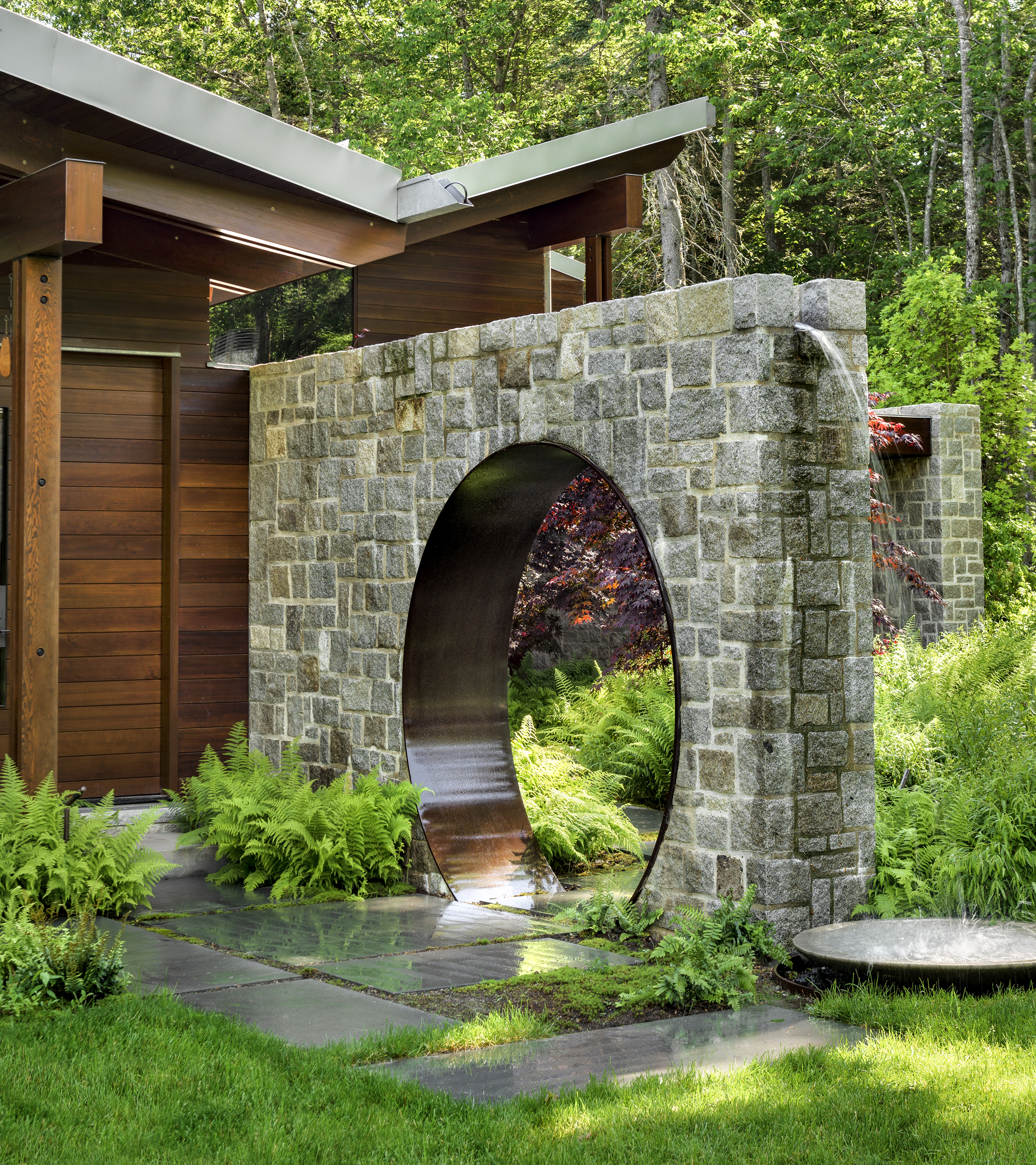 A circular opening in a Corten steel and stone Moon Gate frames the garden
