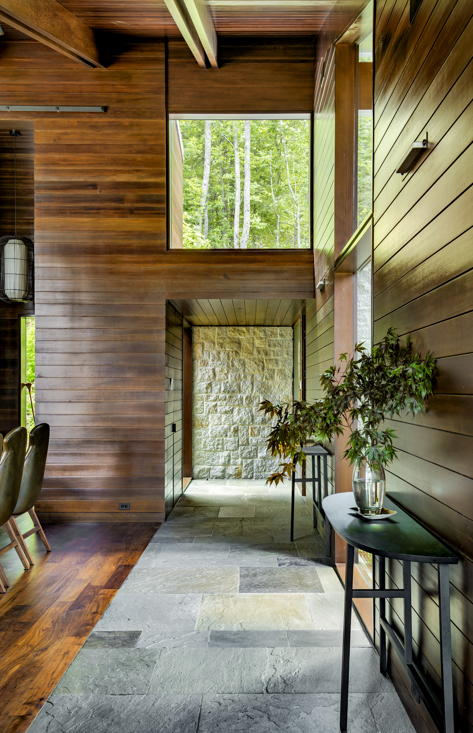 A stone-floored passage ends at a window wall framing the Maine woods