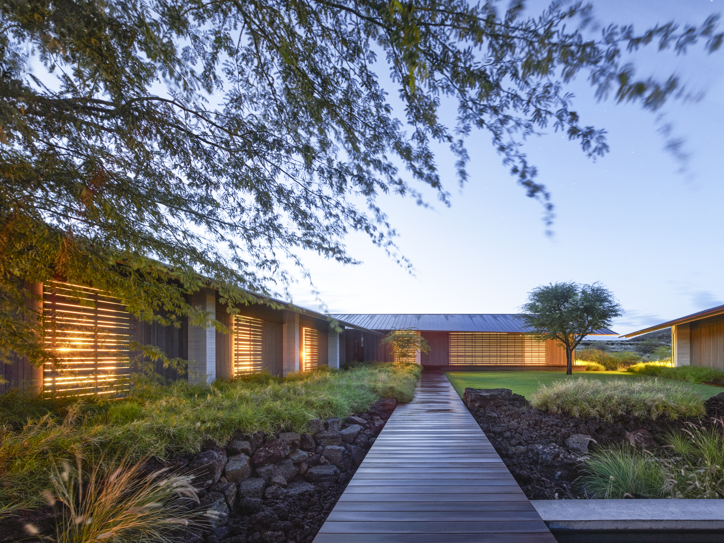Perforated doors glow beside an elevated boardwalk at dusk