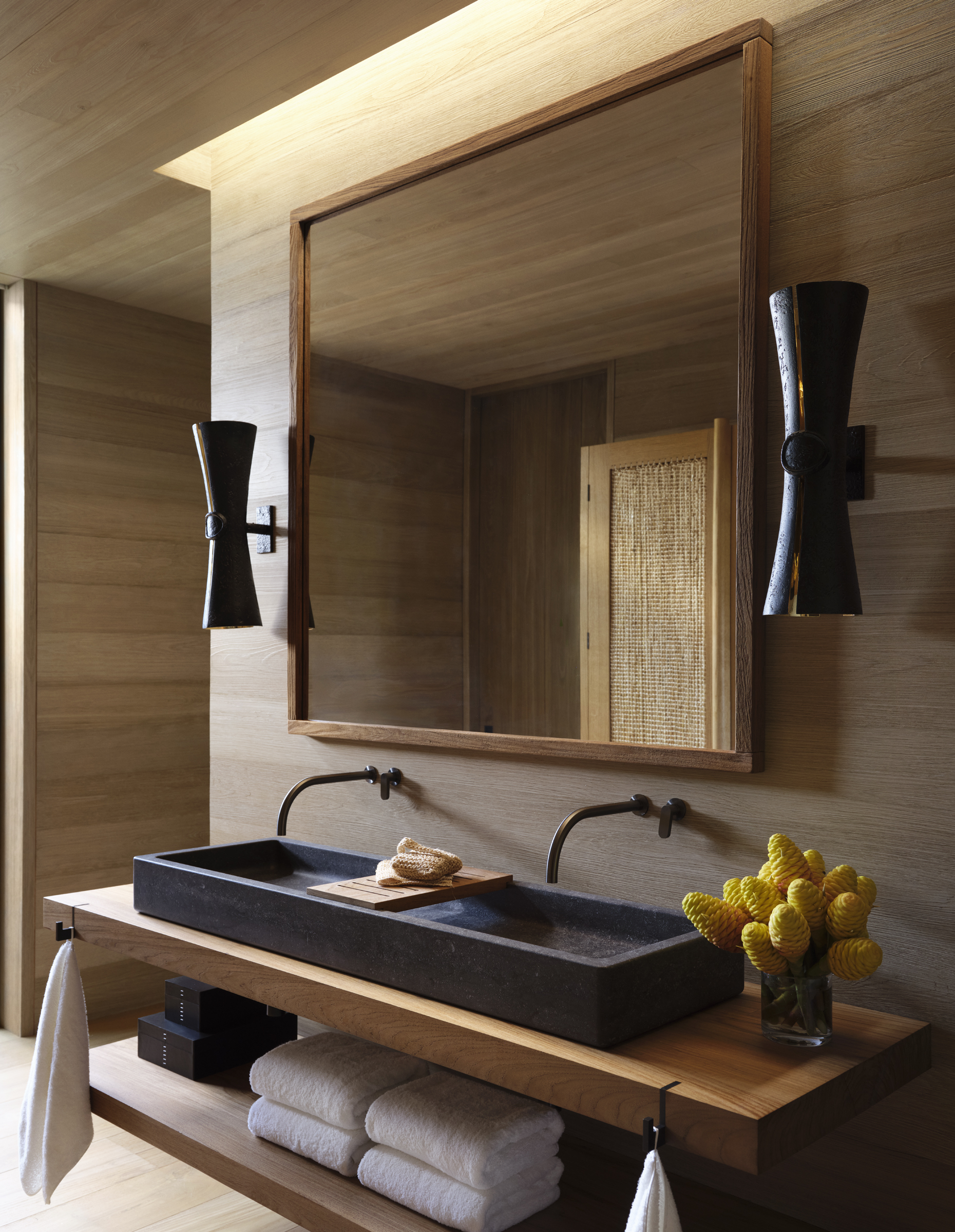 A dark stone trough sink rests on an open teak vanity