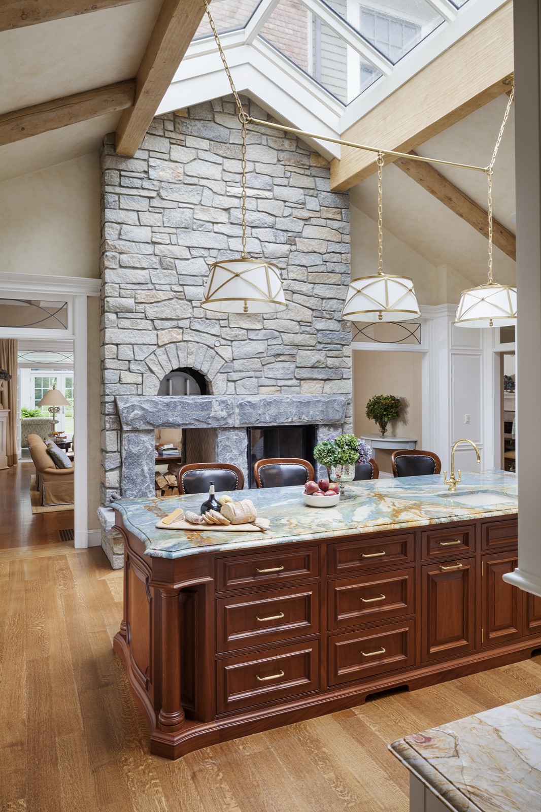 Laurel Woods kitchen island beneath a stone fireplace and skylit beamed ceiling