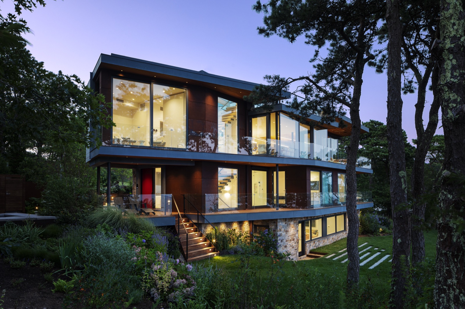 Rear exterior of Miter Point at dusk with lit interiors and a deck above the water