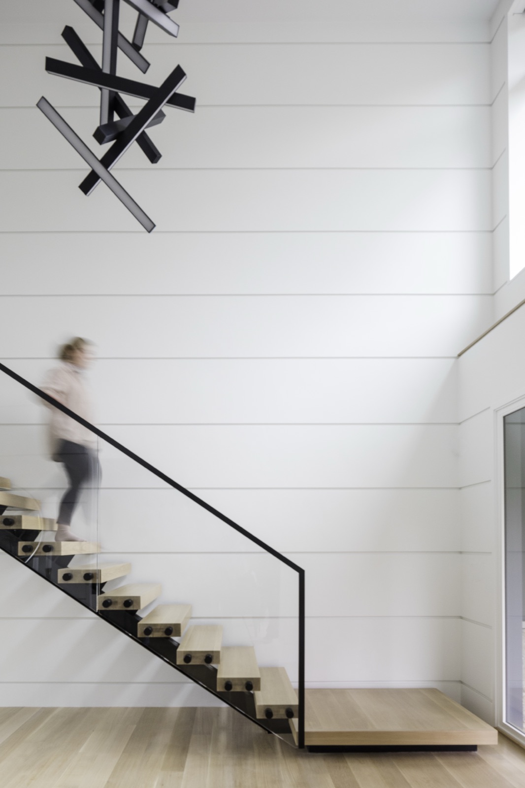 Floating oak stair with a glass rail at Terrace Edge beneath a sculptural light fixture